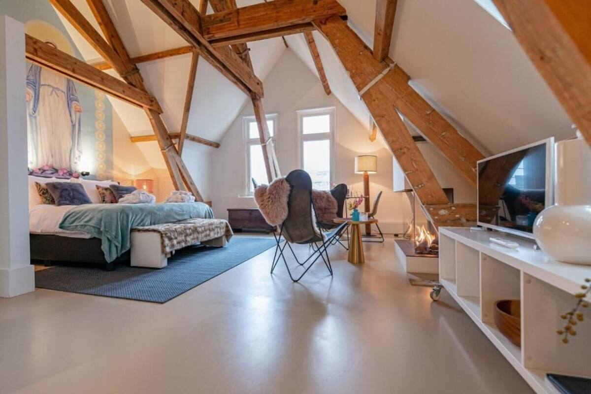 A loft bedroom with a bed, a chair, a TV, and a fireplace.