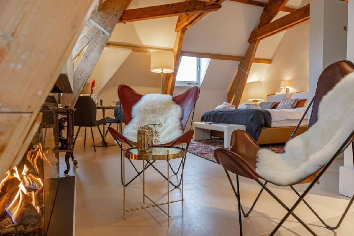 A cozy loft bedroom with a bed, a fireplace, and a dining area with chairs and a table.