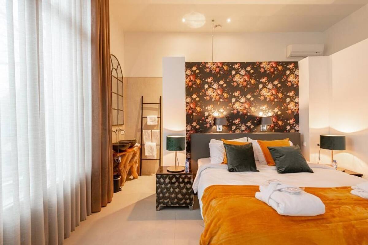 A hotel room with a bed, two bedside lamps, a nightstand, a mirror, and a floral wallpaper.