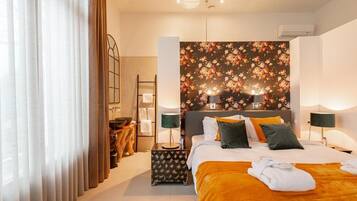 Una habitación de hotel con una cama, dos lámparas de noche, una mesita de noche, un espejo y un papel tapiz floral.
