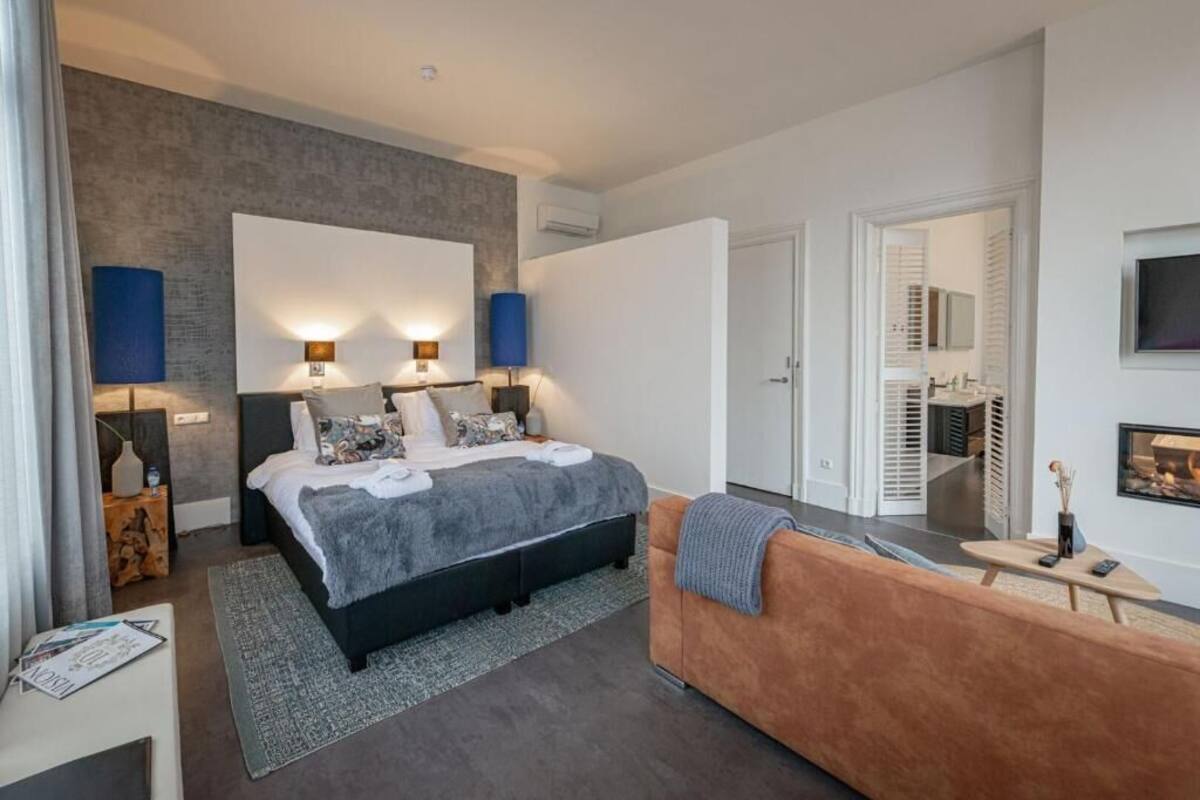 A modern bedroom with a large bed, bedside lamps, a sofa, and a fireplace.