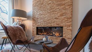 Una habitación acogedora con chimenea, dos sillones de cuero, una mesa redonda y una lámpara.