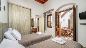 A hotel room with two beds, a wooden ceiling, a TV, and a balcony with a table and chairs. - Villa Yannis in Lindos (Rhodes)