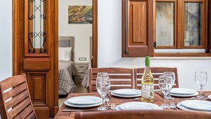 A dining table set with plates, glasses, and a bottle, with wooden chairs and a window with wooden shutters. - Villa Yannis in Lindos (Rhodes)