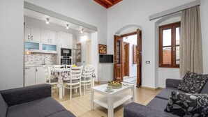 A modern living room with grey sofas, a white coffee table, and a dining area with white chairs and a table. - Villa Yannis in Lindos (Rhodes)