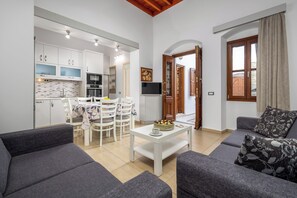 A modern living room with grey sofas, a white coffee table, and a dining area with white chairs and a table. - Villa Yannis in Lindos (Rhodes)