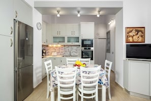 Una cocina moderna con armarios blancos, un refrigerador de acero inoxidable, un horno, un microondas y una mesa de comedor con sillas.