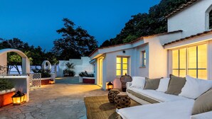 Una zona relax all'aperto accogliente, con un divano bianco, un tappeto tessuto e lanterne.