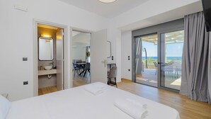 A modern hotel room with a large bed, a bathroom with a sink and mirror, and a balcony with a view.