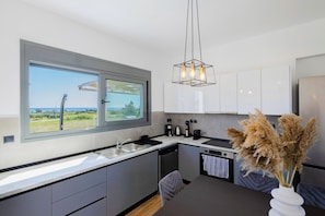 A modern kitchen with a large window, a built-in dishwasher, and a dining area with a table and chairs.
