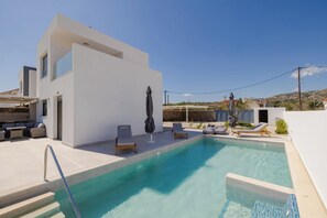 Un espace piscine extérieur moderne, avec un bâtiment blanc, des chaises longues et un ciel bleu azur.