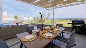 An outdoor dining area with a view of the sea, a grill, and a wicker sofa.