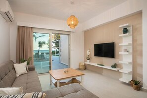 A modern living room with a sofa, a coffee table, a TV mounted on a wall, and a balcony with a view of palm trees. - Sea Homes Villas - Villa Alberto (Rhodes)
