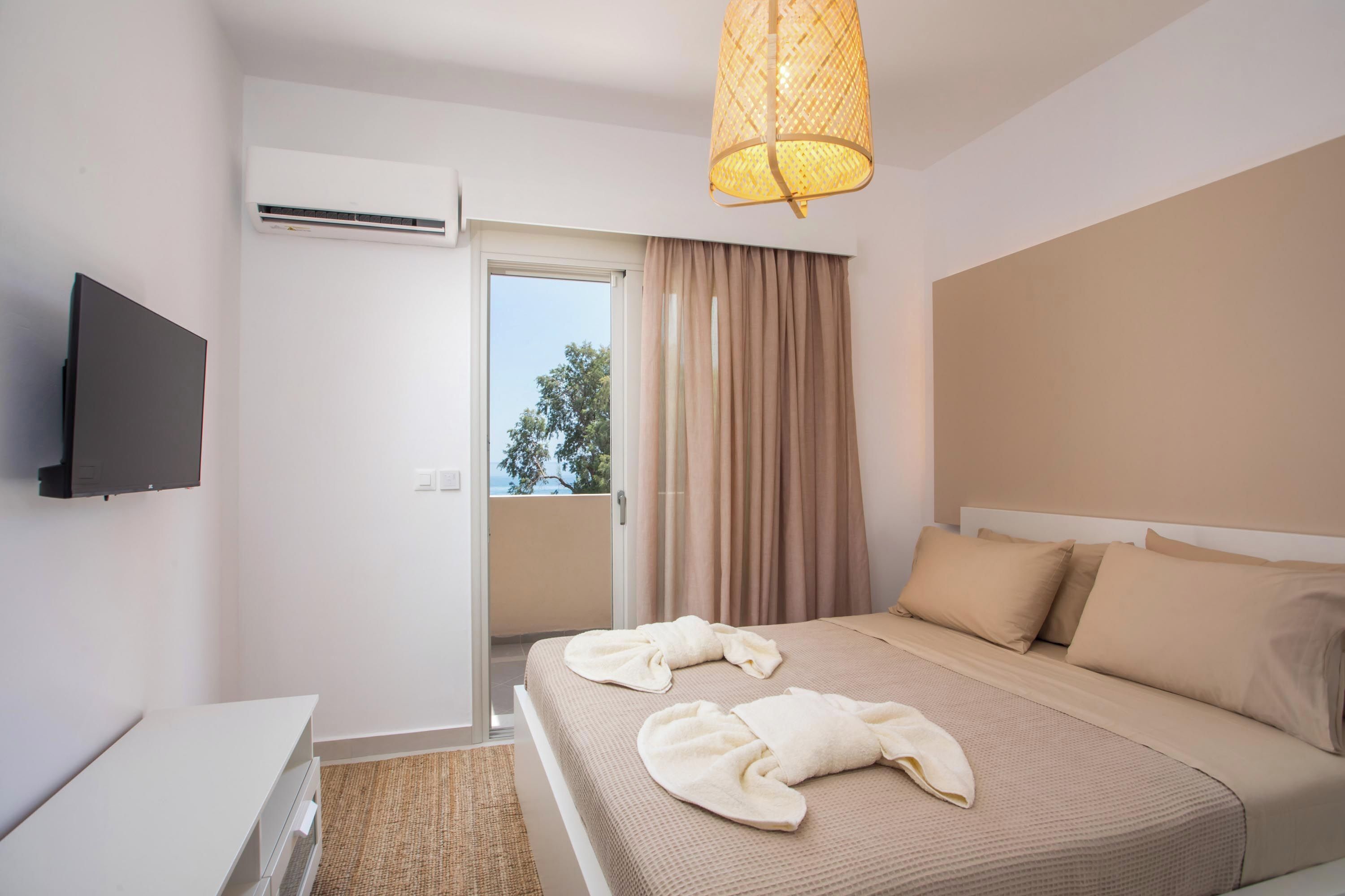A hotel room with a bed, a TV mounted on the wall, and an air conditioning unit.
