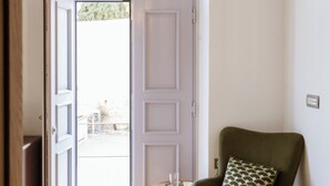 Een kamer met een houten vloer, een groene fauteuil met een gestreept kussen, een klein rond tafeltje met een glas, en een hangende lamp.