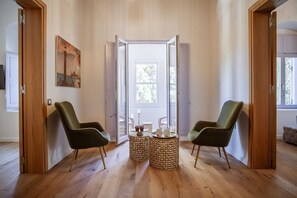 A room with wooden flooring, two green chairs, a table with candles, and a painting on the wall. - Aylin Executive Suites - Sachnisi Suite (Rhodes)