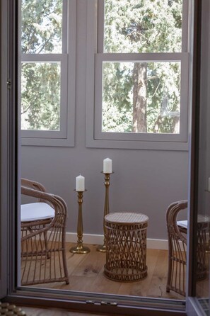 A room with a view of trees through large windows, wicker chairs, a round table, and two candle holders. - Aylin Executive Suites - Sachnisi Suite (Rhodes)
