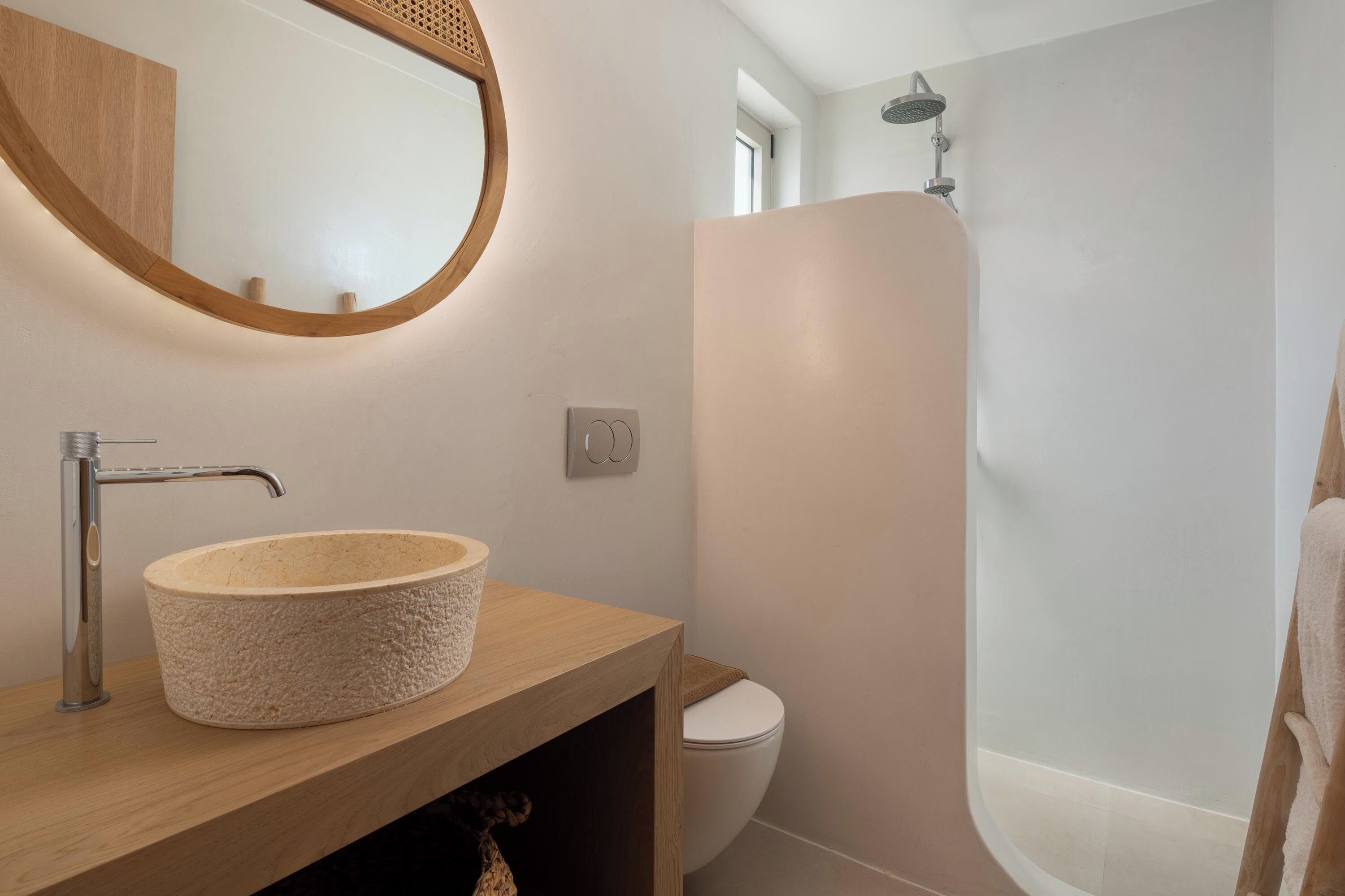 A bathroom with a round basin, a toilet, and a shower.