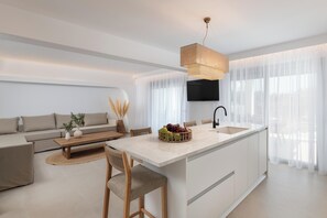 Eine moderne Küche mit einer zentralen Kochinsel, einem Essbereich mit Stühlen, einer Couch und einem an der Wand befestigten Fernseher.