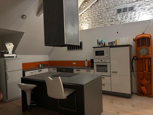 A modern kitchen with a central island, built-in appliances, and a stone wall.