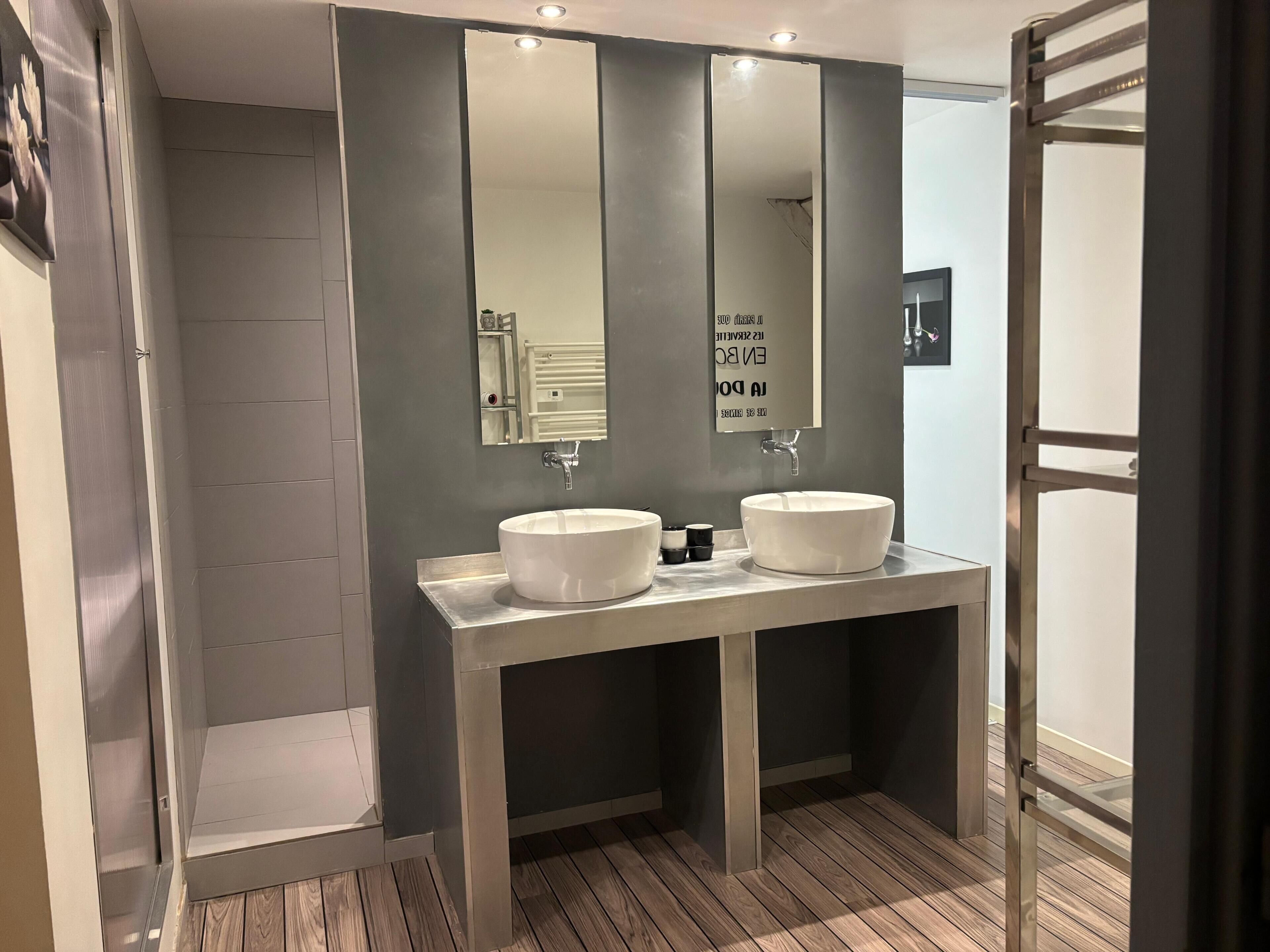 Een moderne badkamer met twee wastafels, een grote spiegel en een douche.