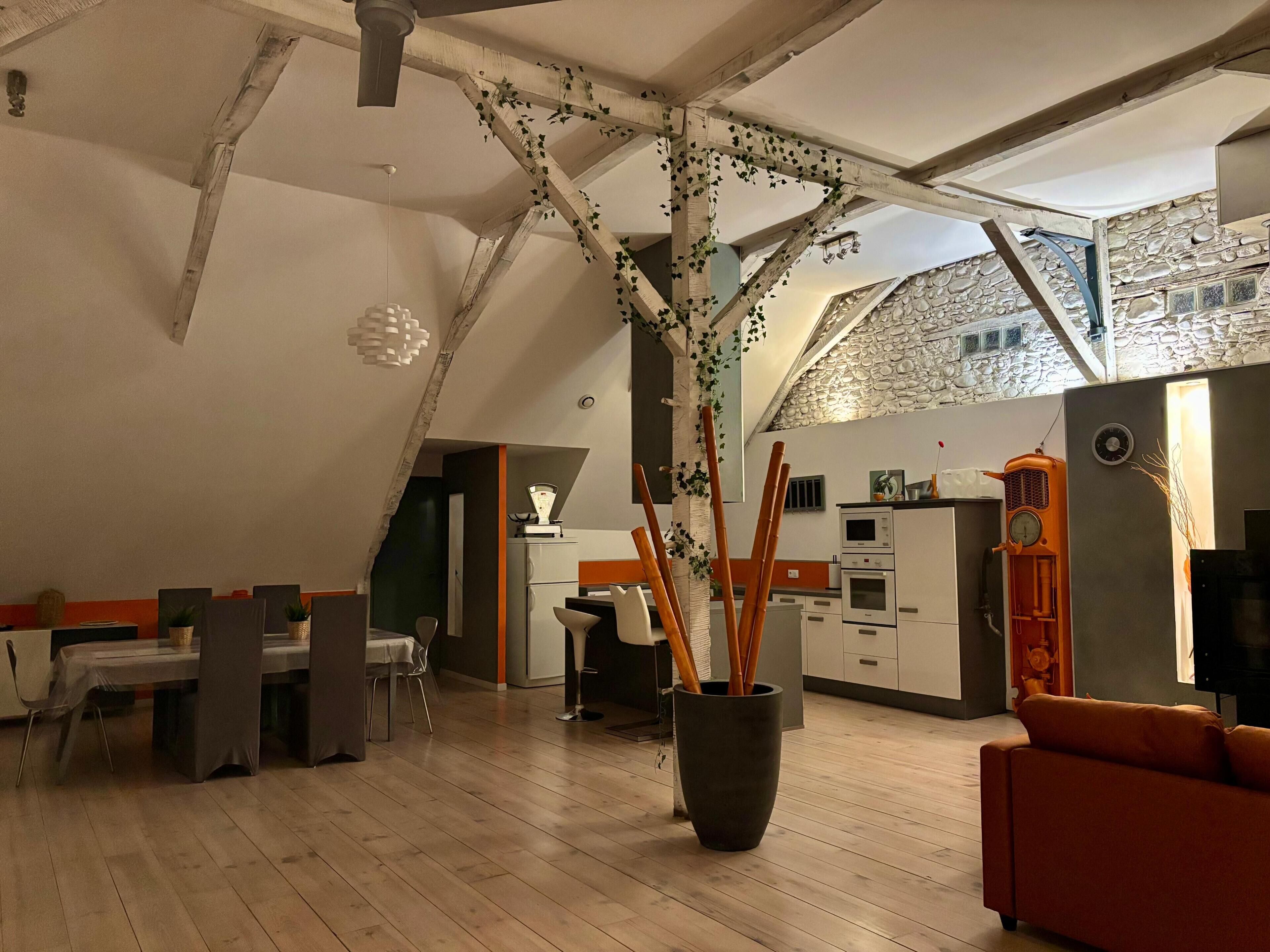 A modern kitchen with a stone wall, a dining area with a table and chairs, and a large potted plant.