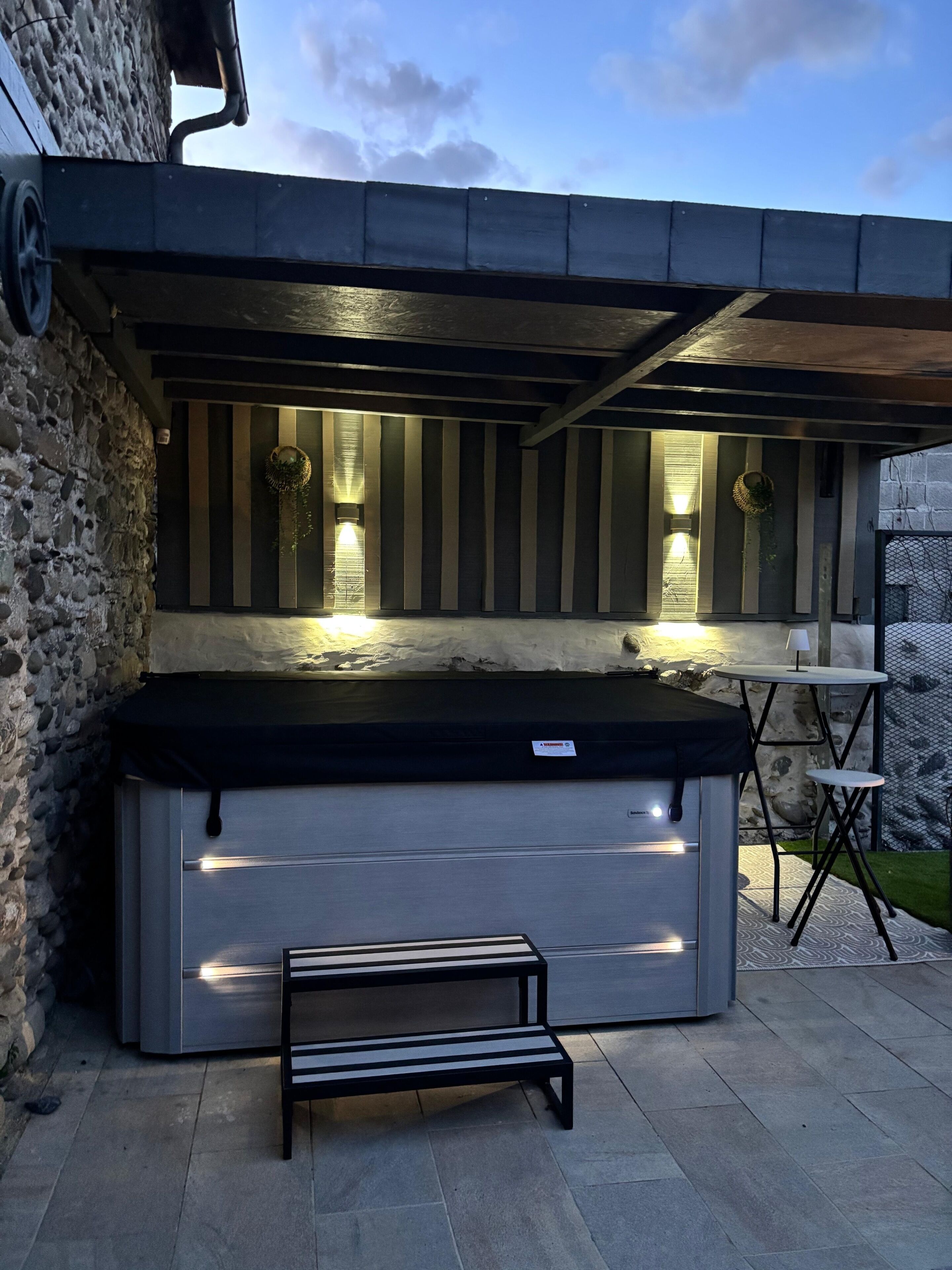 A hot tub with a bench, a stone wall, and a view of the sky.