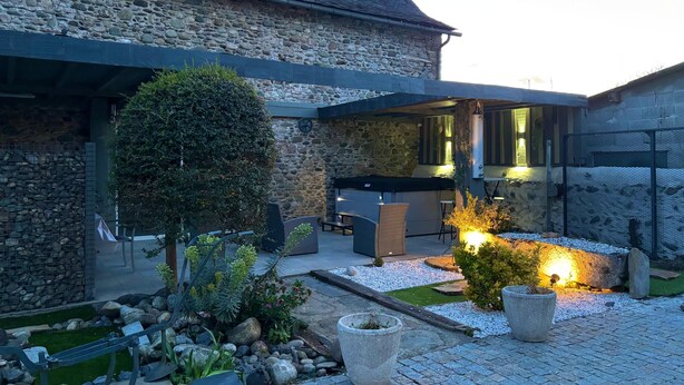 Ein Steinhaus mit moderner Terrassenanlage, Außenmöbeln und einem gut beleuchteten Garten.