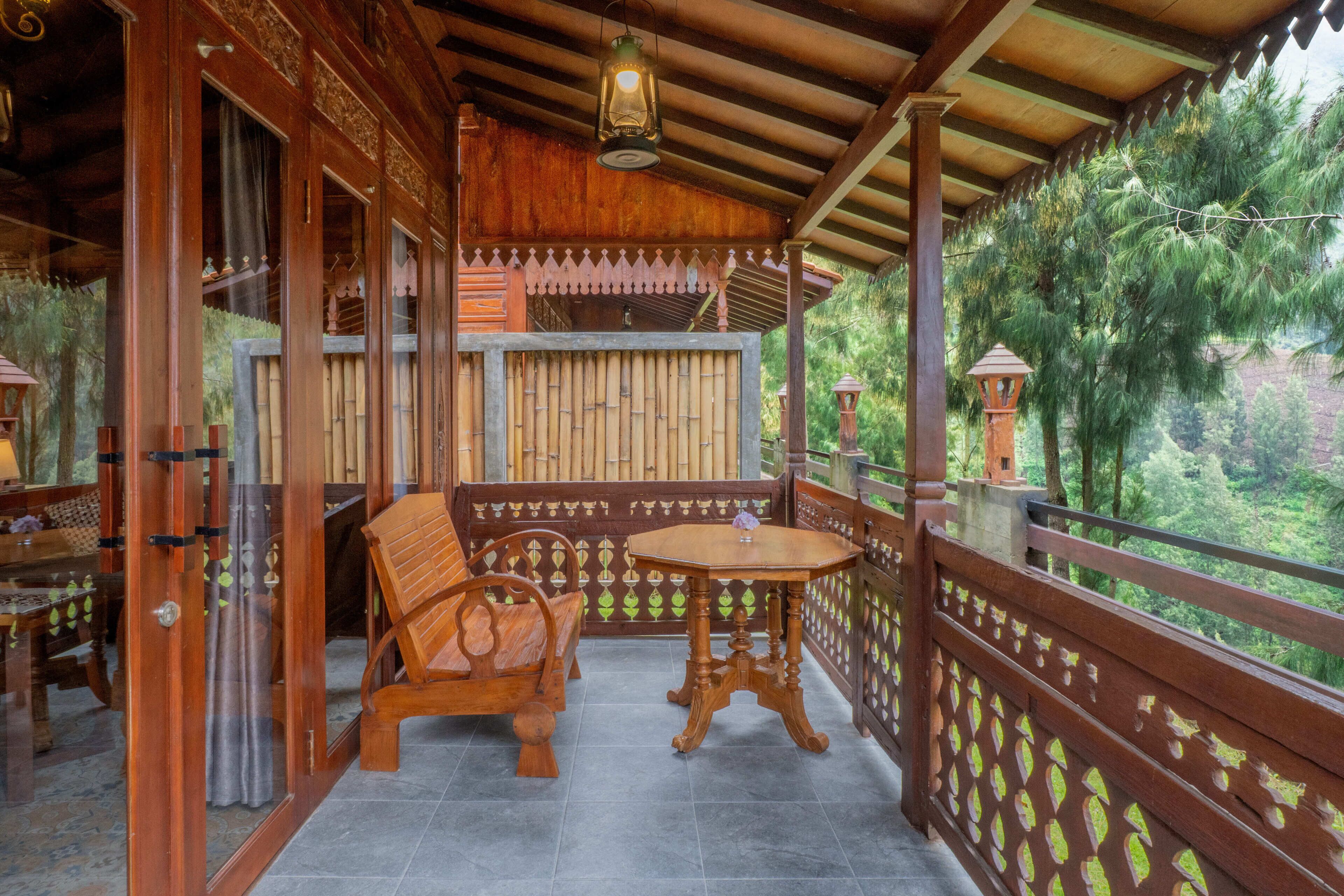 A covered balcony with wooden furniture, a table, and a view of greenery.