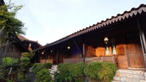 Un edificio de madera tradicional con entrada de tejas, rodeado de abundante vegetación y un sendero de piedra.