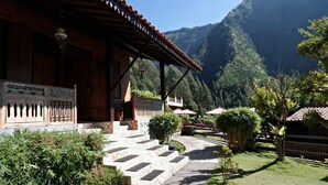 Un edificio tradicional de madera con techo de tejas, una escalera de piedra que lleva a la entrada y vistas a un paisaje montañoso.