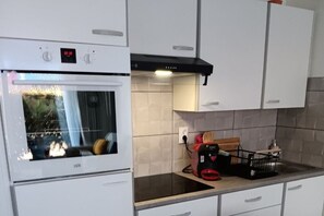 A kitchen with a built-in oven, a range hood, and a countertop with a toaster and a kettle. - GROUND FLOOR TERRACE NEAR THE SEA (STELLA PLAGE)