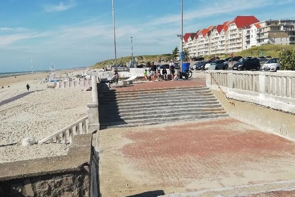 A beachside hotel with a parking area, a pedestrian walkway, and a view of the beach.