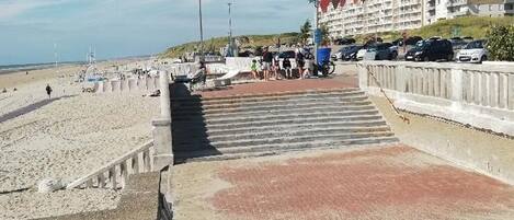 A beachside hotel with a parking area, a pedestrian walkway, and a view of the beach.