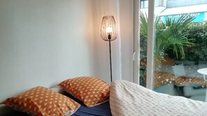 Ett sovrum med en säng, två kuddar, en golvlampa och utsikt över en trädgård genom en glasdörr.
