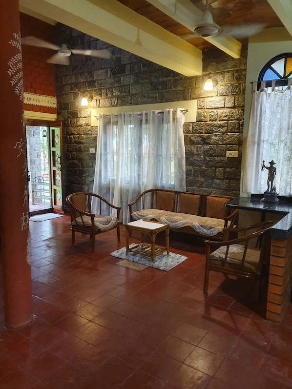 Une pièce chaleureuse avec un mur en pierre, un banc en bois, deux chaises, une petite table et un ventilateur de plafond.