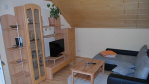 Ett modernt vardagsrum med ett TV-bord i trä, en platt-TV, ett soffbord i trä, en grå soffa och ett skåp i trä med glasdörrar.