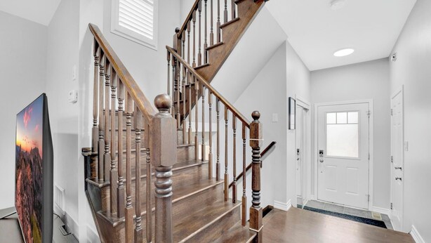 A staircase with wooden balusters and a handrail, a door with a window, and a flat-screen TV on a stand. - Entire2Storey+Trampoline+65"+EnclosedYard (Kitchener)