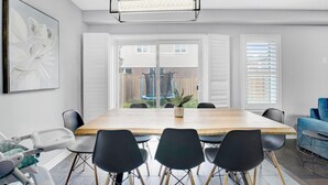 A modern dining room with a large wooden table, black chairs, a hanging light fixture, and a view of a backyard through large windows. - Entire2Storey+Trampoline+65"+EnclosedYard (Kitchener)