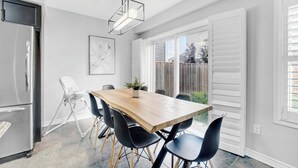 A modern kitchen with a stainless steel refrigerator, a wooden dining table with black chairs, a pendant light, and a view of the backyard through large windows. - Entire2Storey+Trampoline+65"+EnclosedYard (Kitchener)