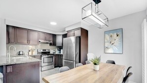 A modern kitchen with dark cabinets, stainless steel appliances, a wooden dining table, and a potted plant. - Entire2Storey+Trampoline+65"+EnclosedYard (Kitchener)