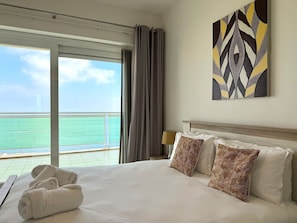Ein Hotelzimmer mit Bett, Kissen, einem Gemälde und Blick auf das Meer.