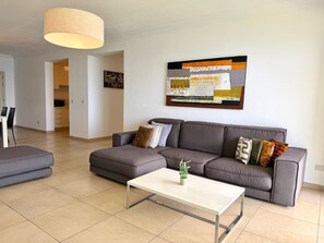Ein modernes Wohnzimmer mit einem grauen Sofa, einem weißen Couchtisch und einem großen abstrakten Gemälde an der Wand.