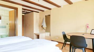 A hotel room with a bed, a desk, a chair, and a small table with a vase.