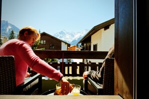 A person pouring a drink into a glass on a balcony with a mountain view. - Alpia FlexiHomes (Graechen)