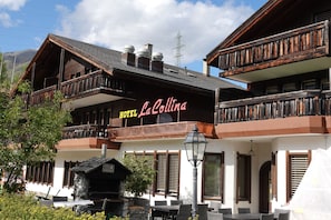 Un hĂŽtel Ă la façade en bois, dotĂ© de balcons, dâune terrasse et dâune enseigne indiquant « HĂTEL La Collina ».