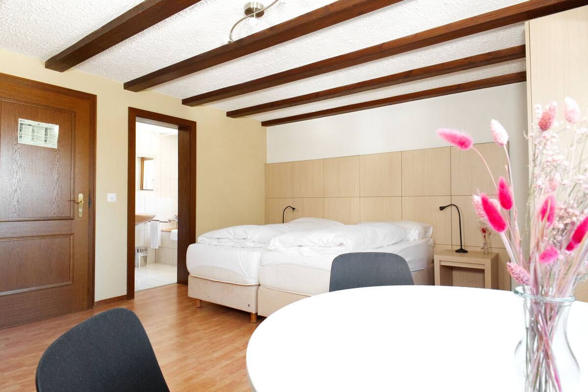 Un dormitorio con una cama, una mesita de noche, una silla y un florero con flores.