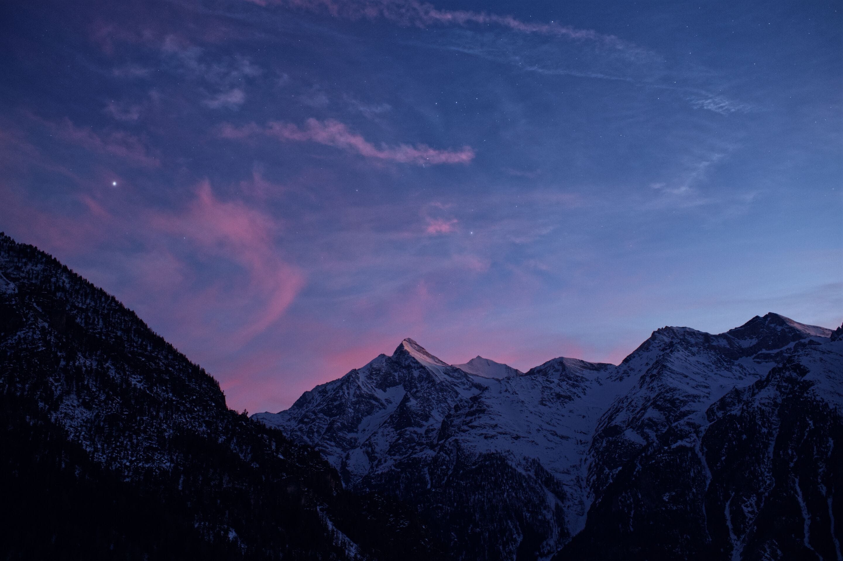 Une chaîne de montagnes aux sommets enneigés, sous un ciel crépusculaire.