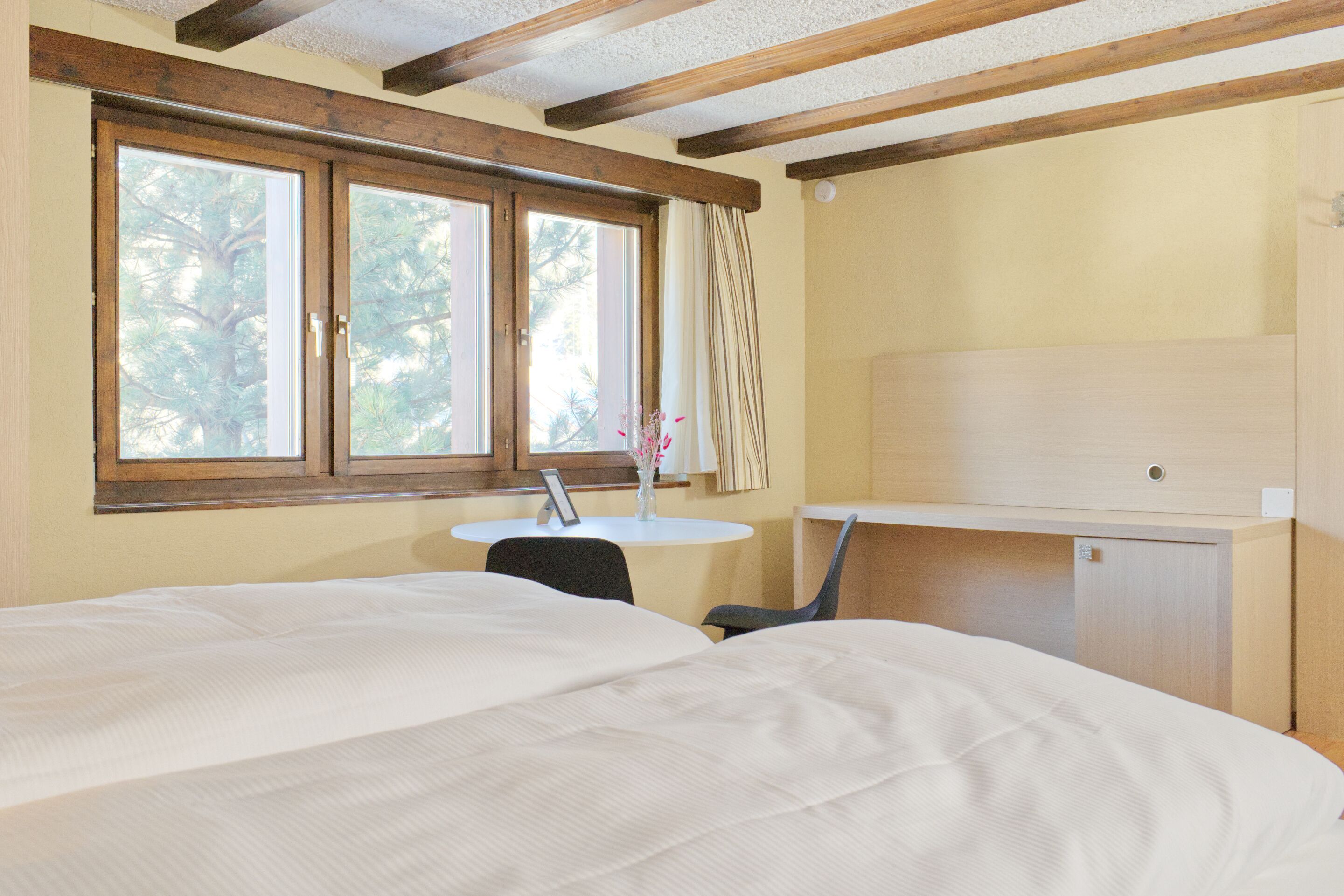 Una habitación con cama, escritorio, silla, una mesita y ventana con cortinas.