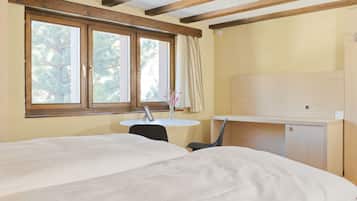 A room with a bed, a desk, a chair, a small table, and a window with curtains.